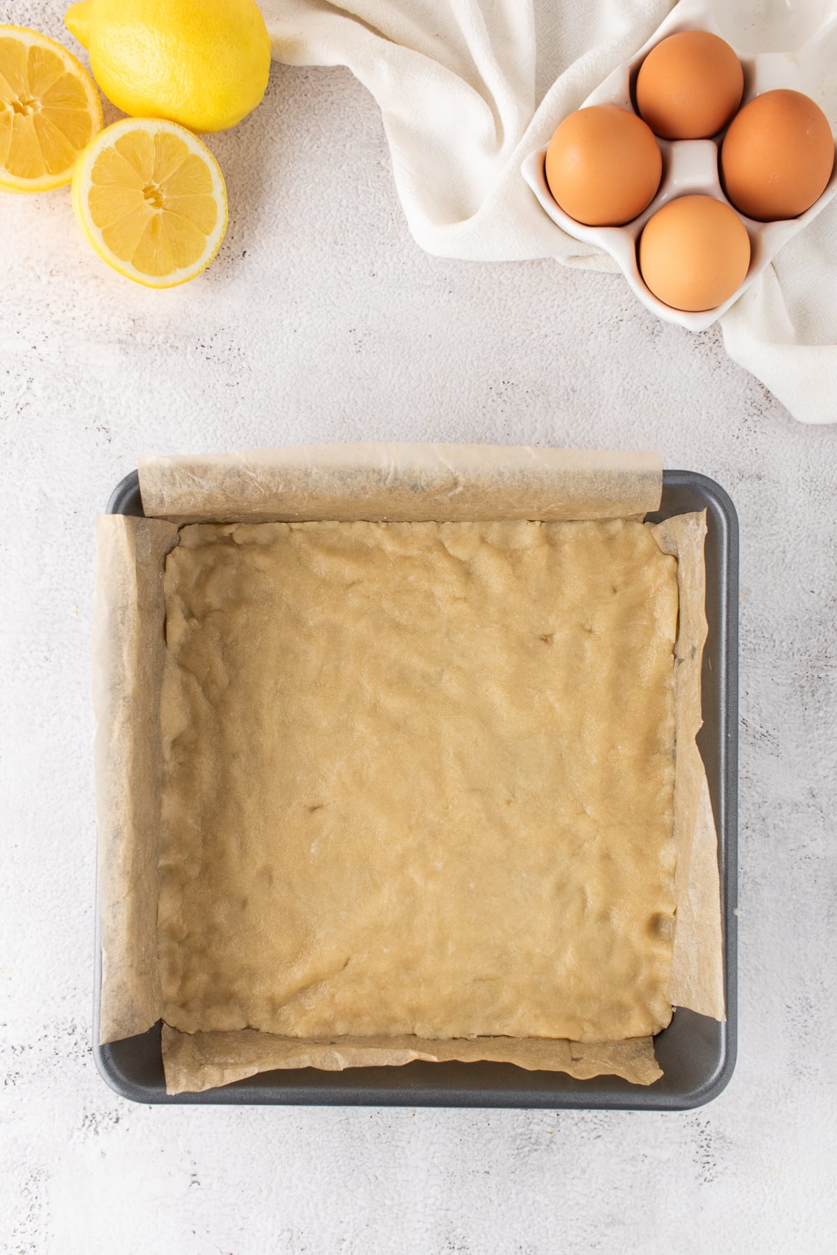 Shortbread cookie crust pressed evenly into a parchment-lined square baking pan.