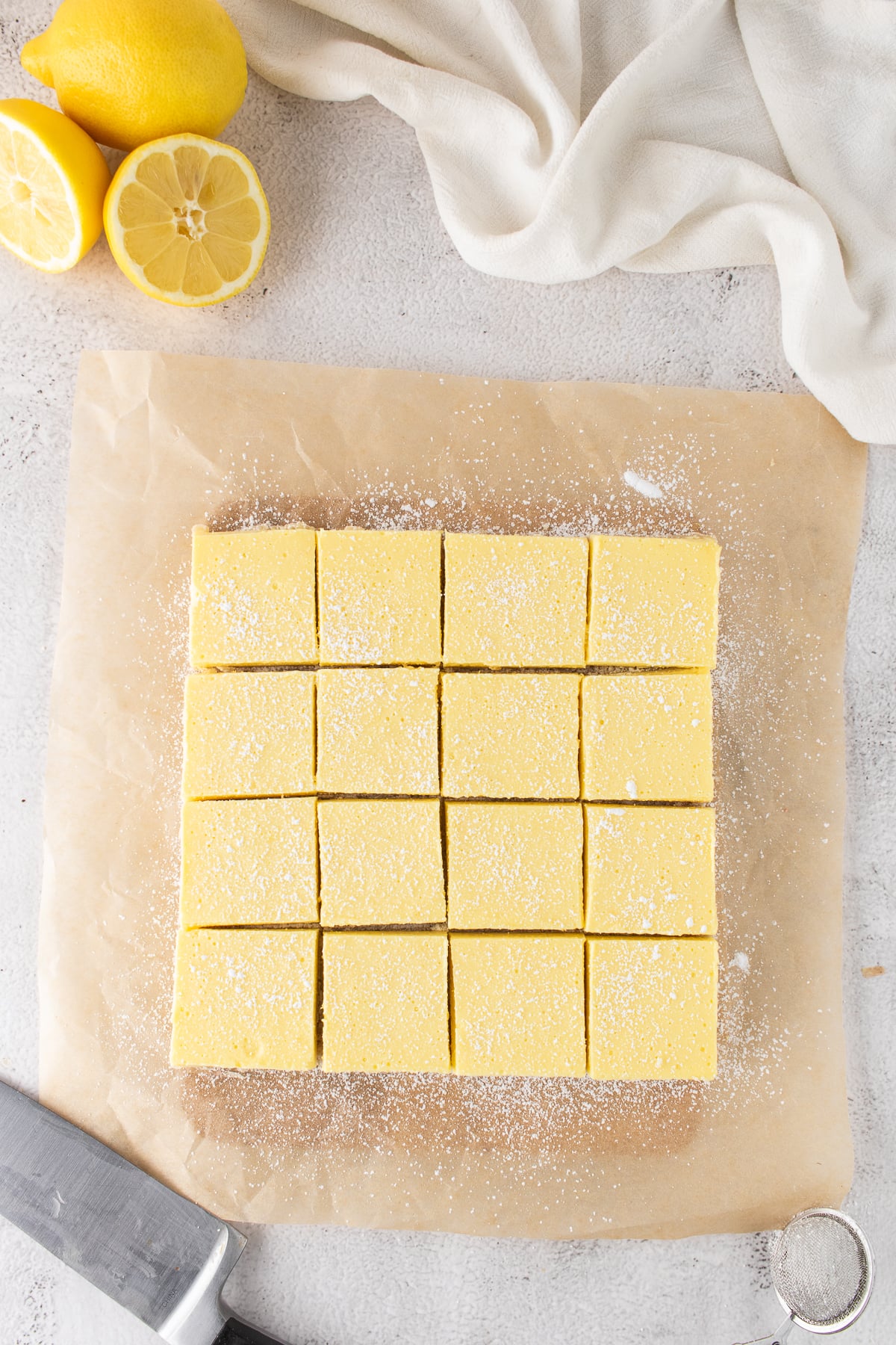 Lemon bars sliced into squares on parchment and dusted with powdered sugar.