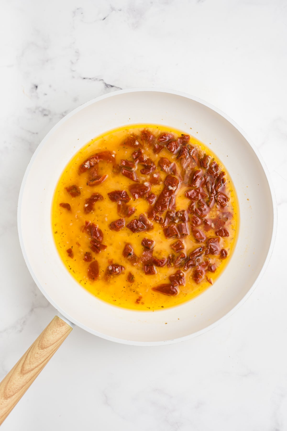 Garlic and sun-dried tomatoes cooking in a skillet with chicken broth for the creamy sauce.