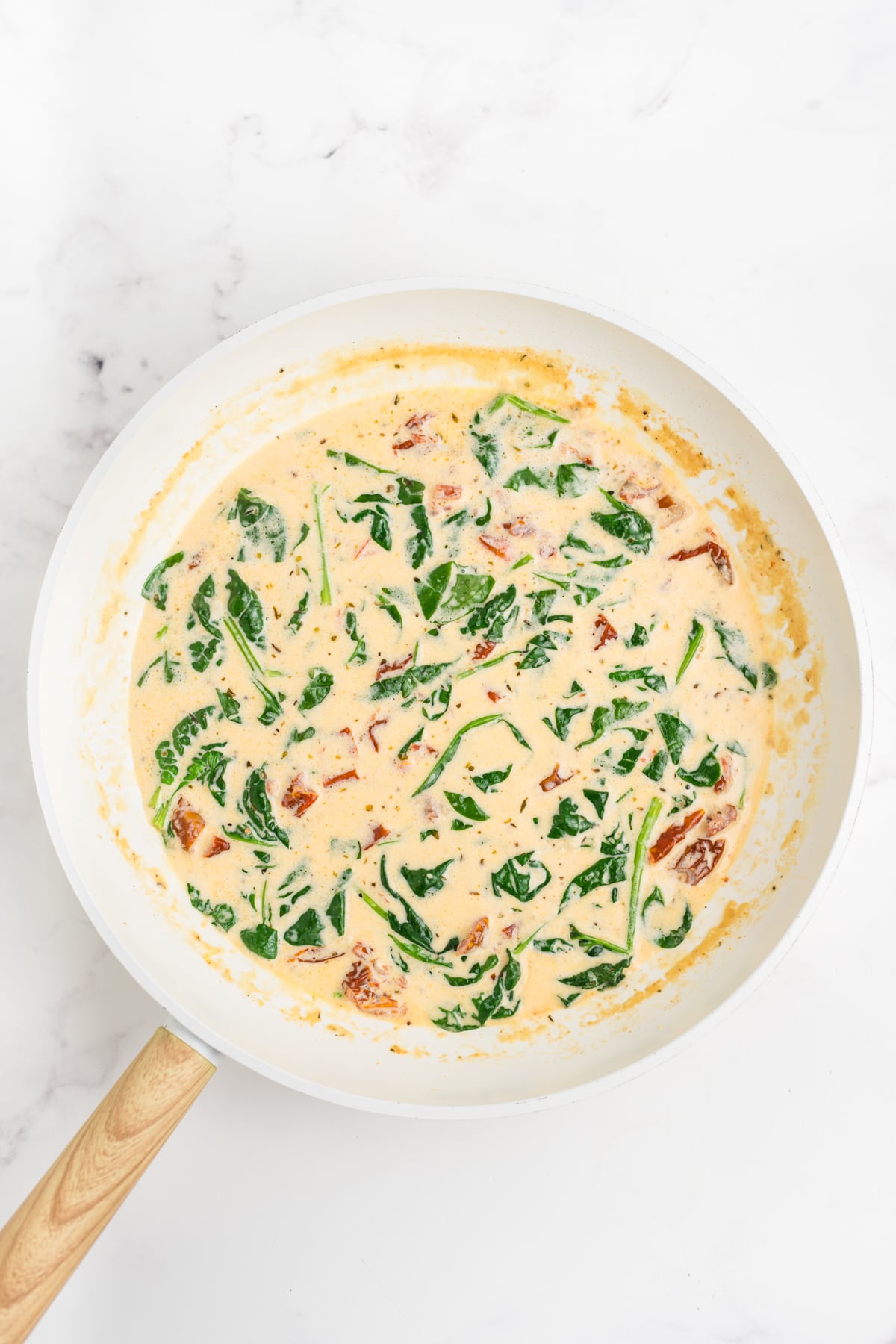 Creamy Parmesan sauce with sun-dried tomatoes and spinach simmering in a skillet.