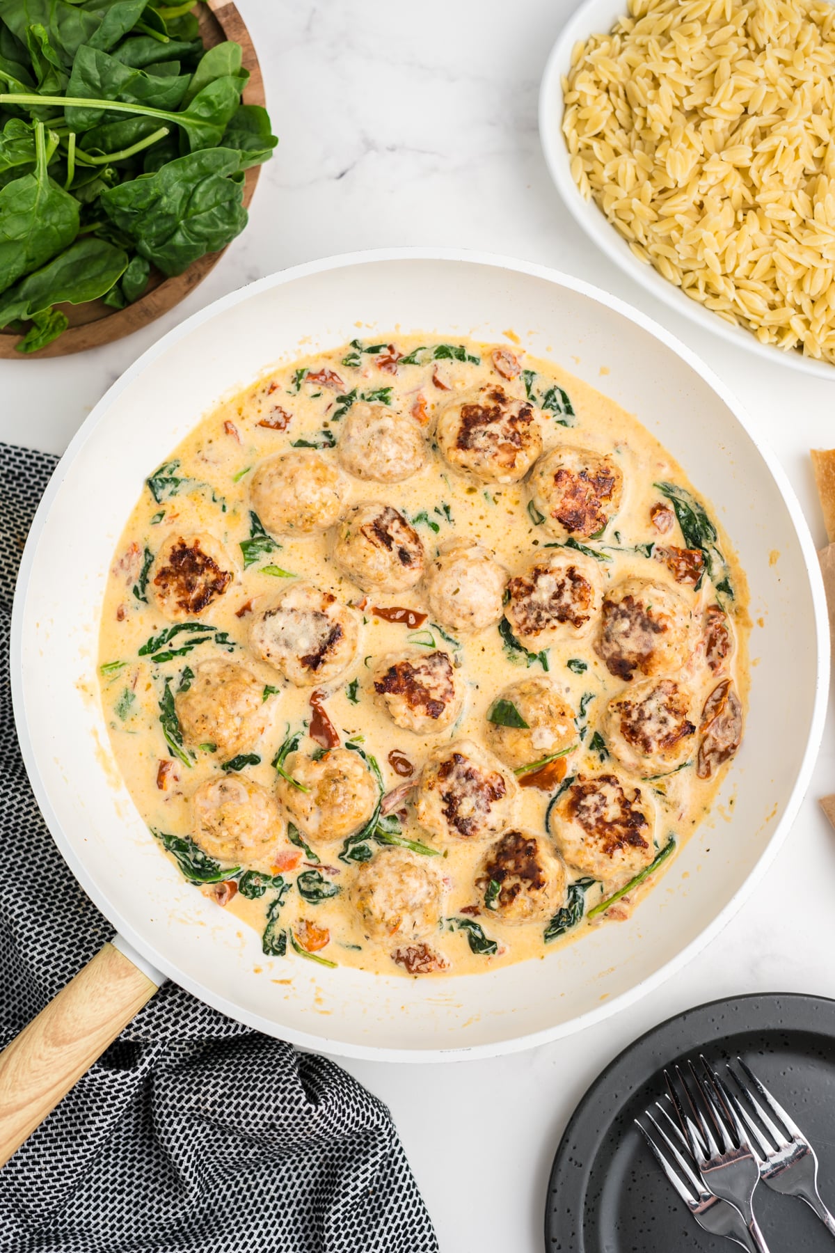 Chicken Meatballs simmering in creamy Parmesan sauce with spinach and sun-dried tomatoes.