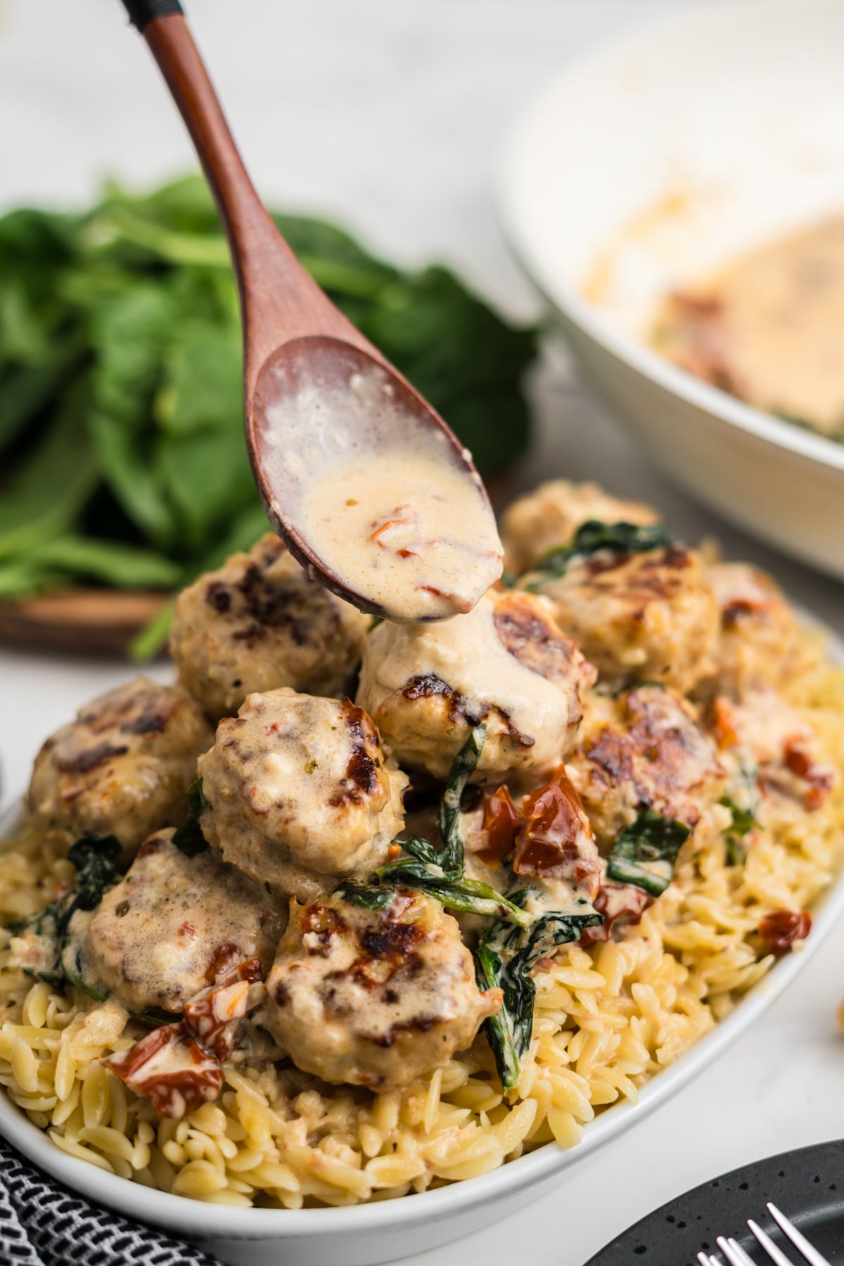 Creamy sauce drizzled with a wooden spoon on top of a serving plate of meatballs on a bed of orzo.