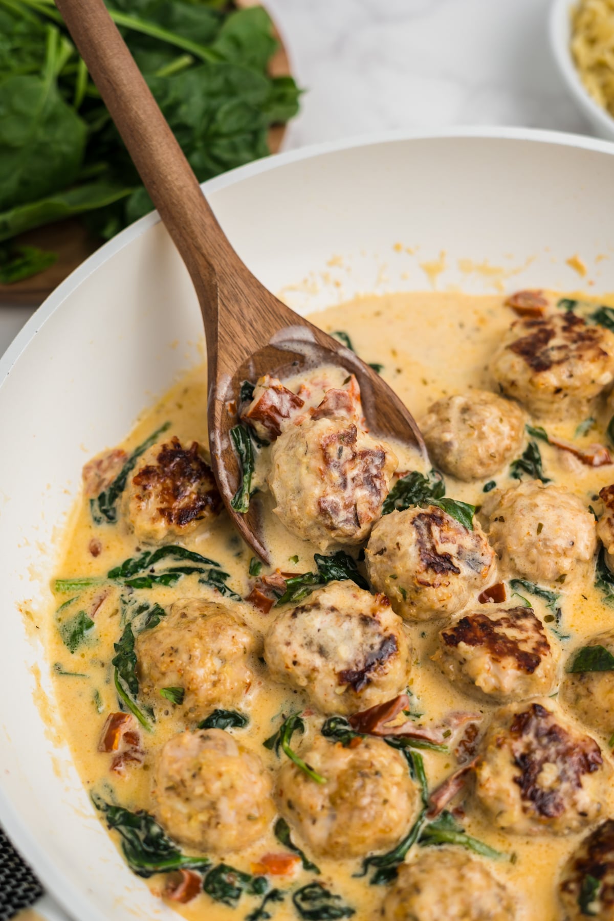 A skillet with a wooden spoon lifting some meatballs up.