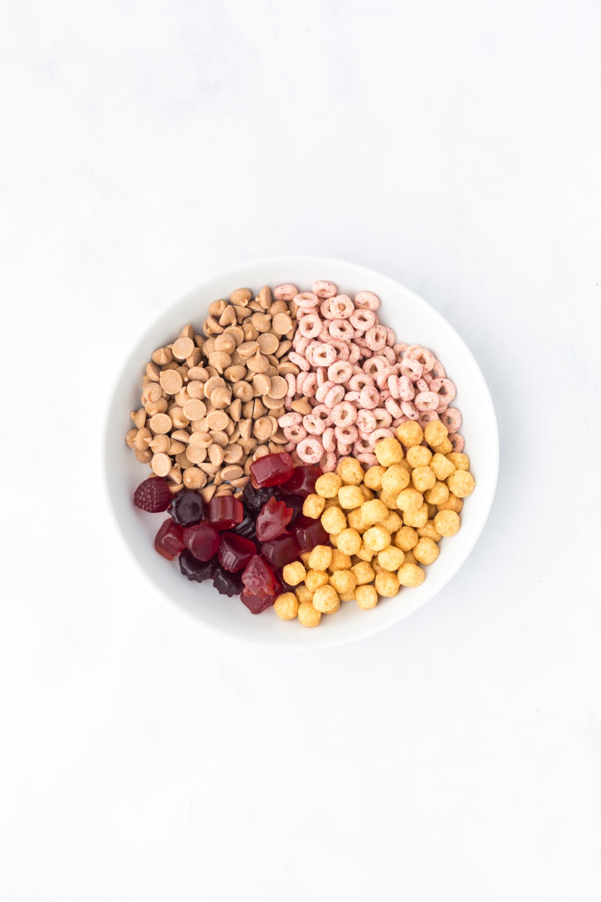 Berry cereal, peanut butter cereal, fruit snacks, and peanut butter chips in a mixing bowl.