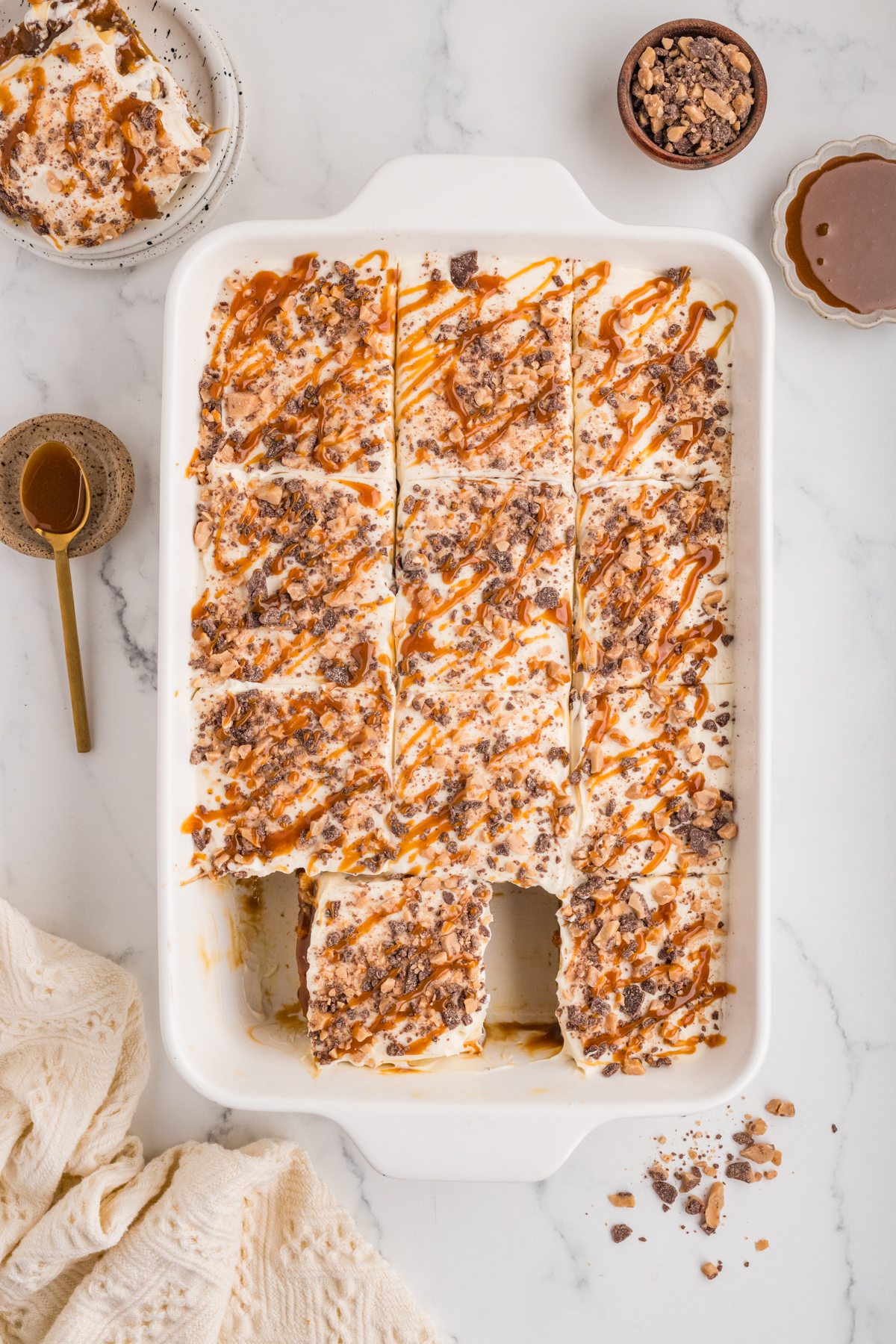 Finished cake topped with cream cheese whipped cream, toffee bits, and caramel drizzle missing a slice.