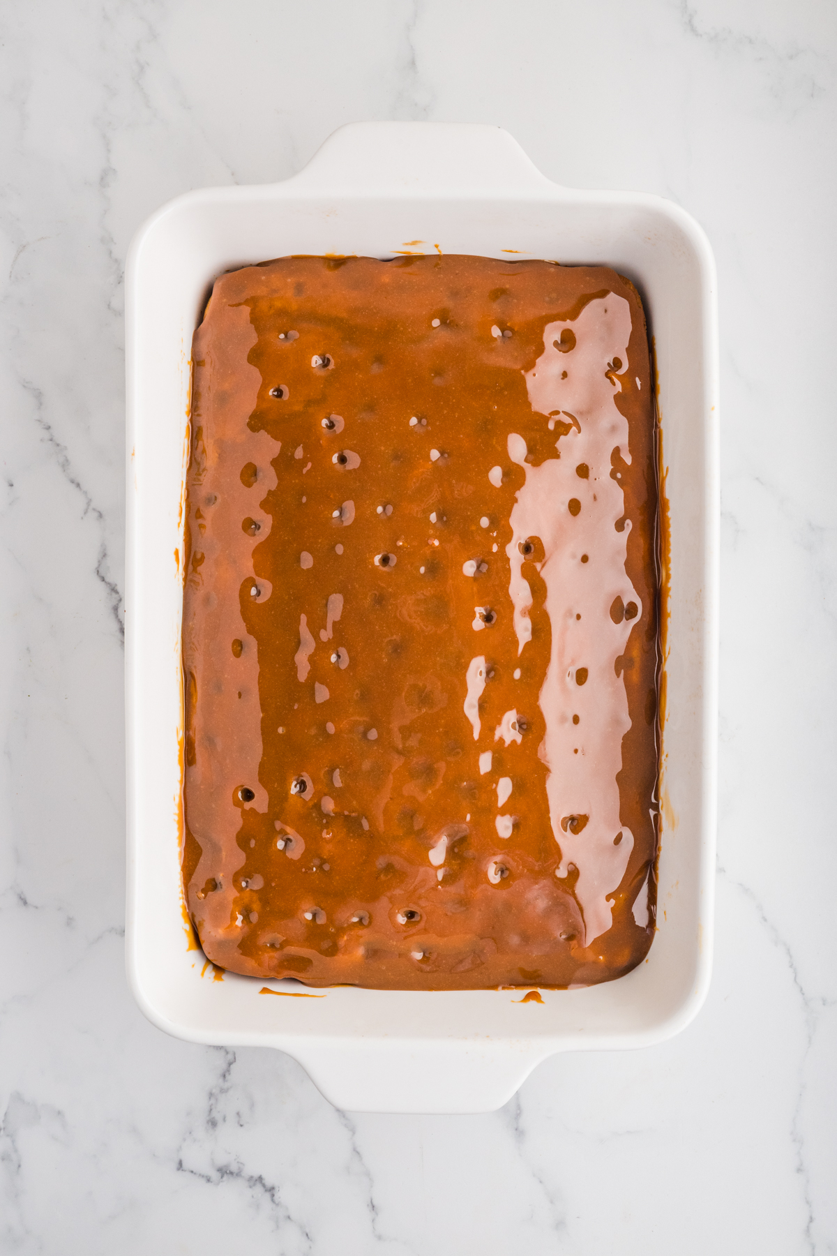 Baked cake with holes poked and caramel covering entire surface.