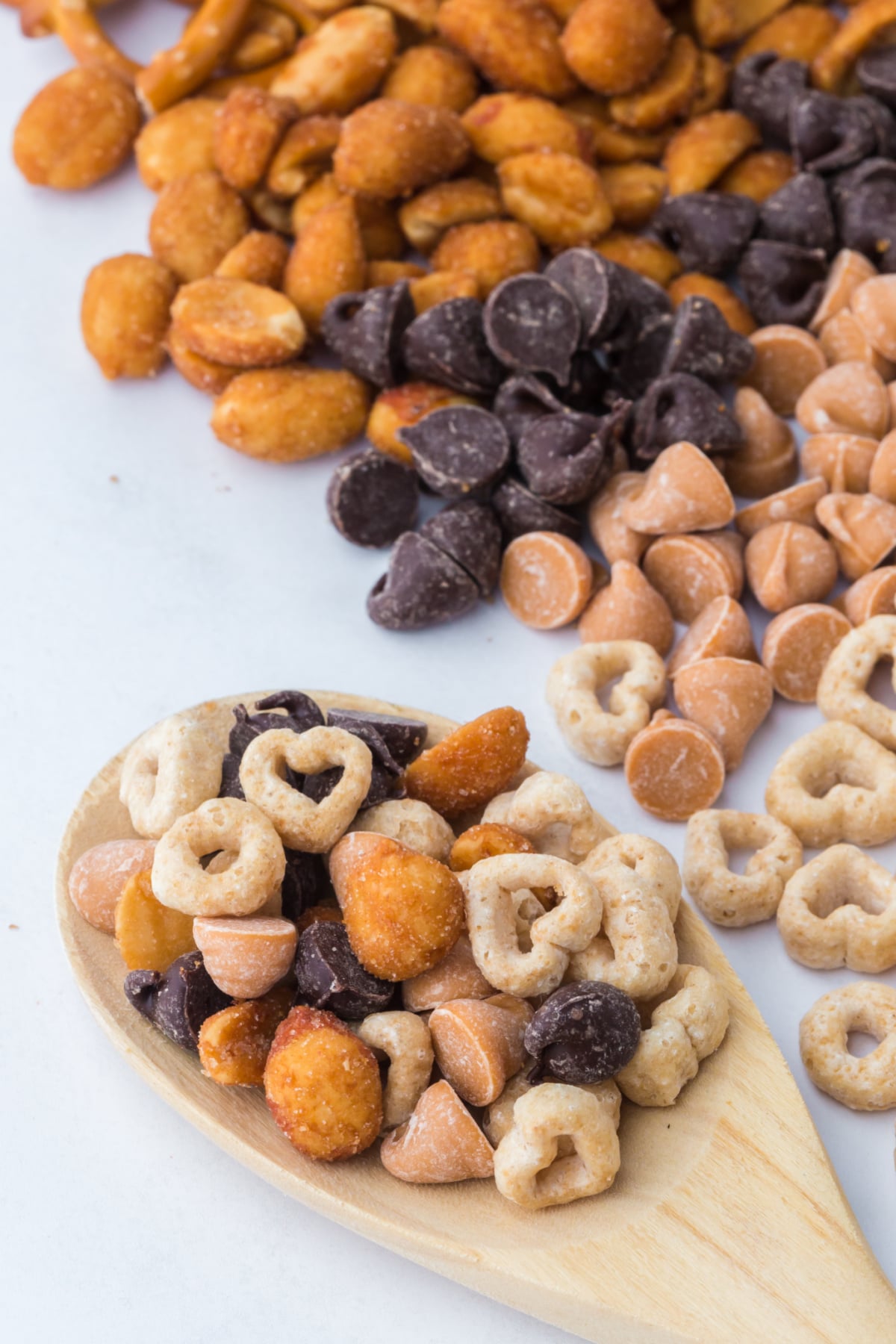 A wooden spoonful of snack mix on table beside rows of trail mix ingredients.