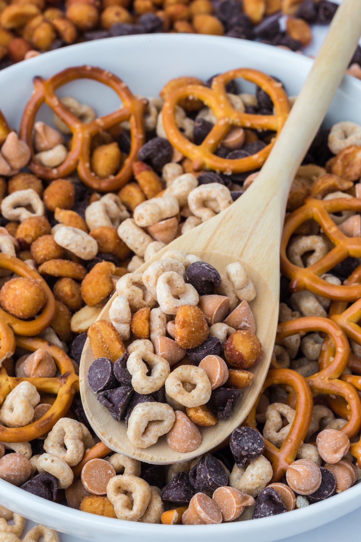 A wooden spoonful of trail mix resting on a bowlful.