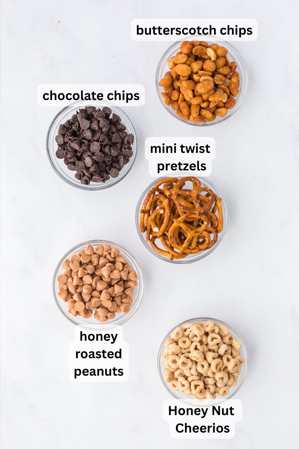 All of the ingredients needed to make sweet and salty trail mix in bowls on a table.