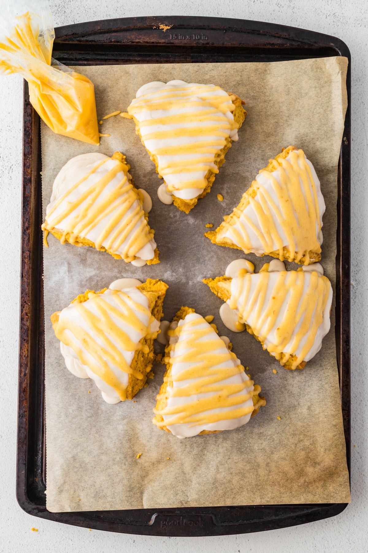 Pumpkin drizzle added to top of cooled scones on baking sheet.