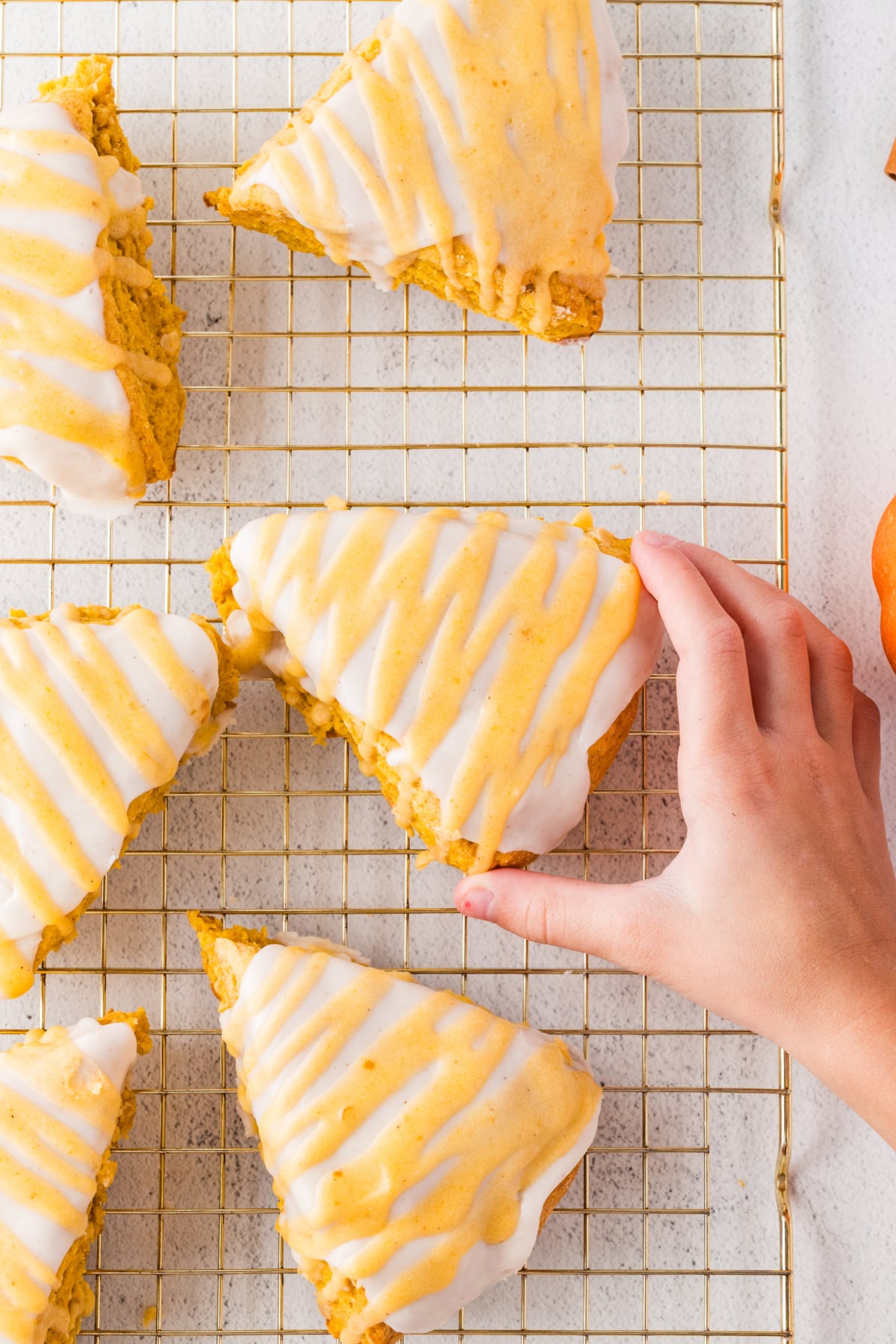 Iced scones on a rack with one being picked up.