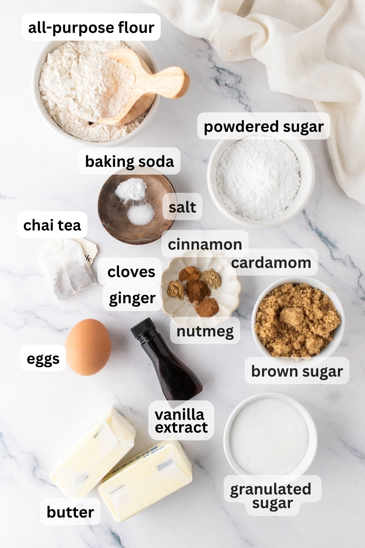 All of the ingredients needed to make chai cookies in bowls on a table.