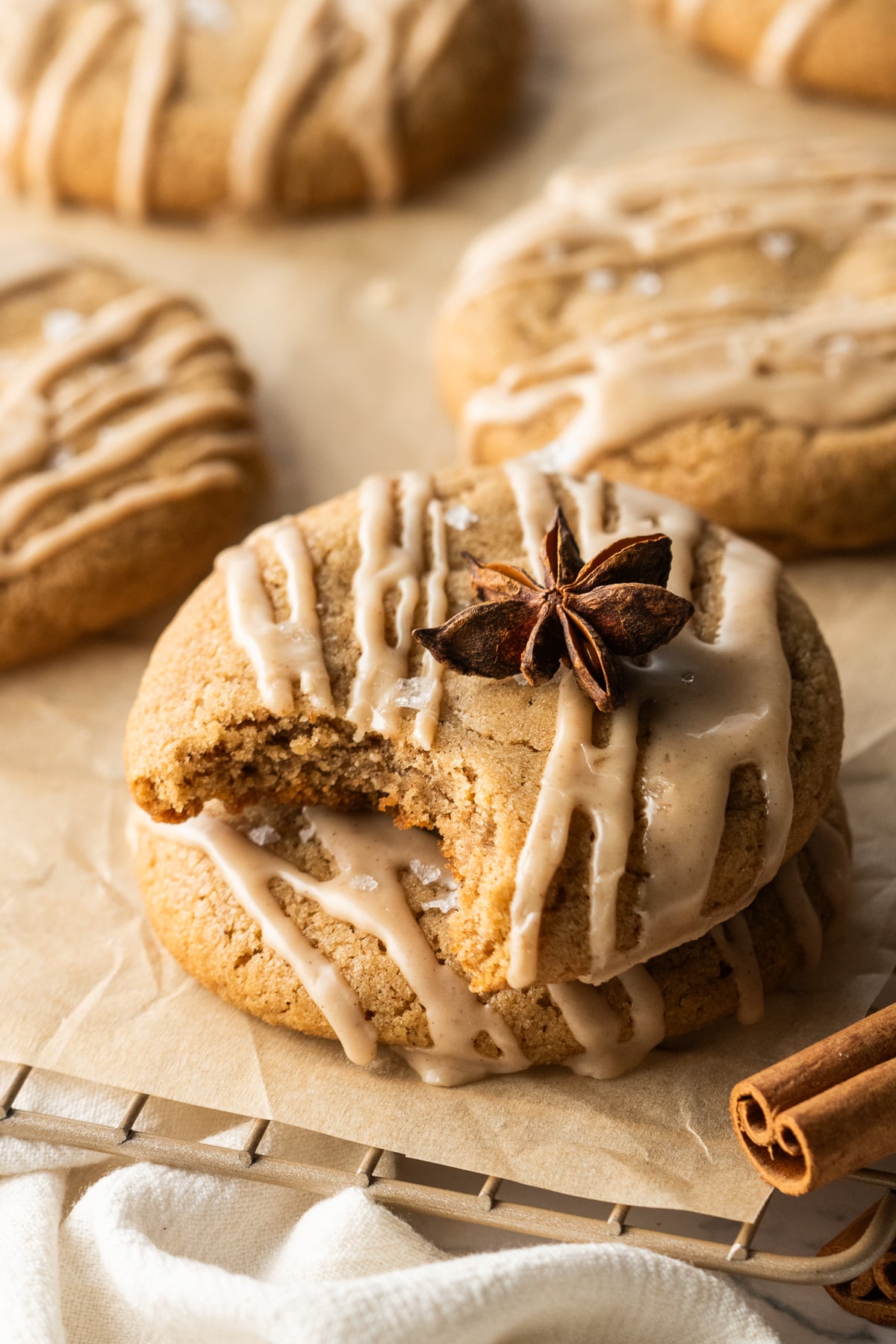 A cookie missing a bite on top of another cookie with a star anise on top on a parchment covered rack.
