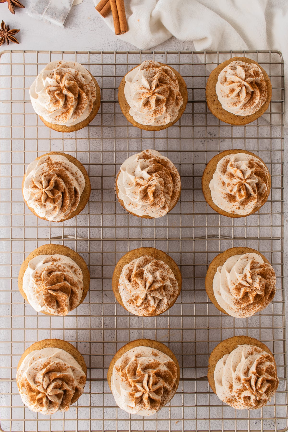 Cupcakes topped with piped buttercream and cinnamon on a wire rack.