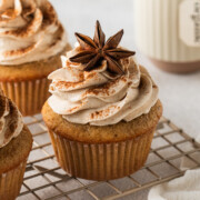 Chai cupcakes with buttercream frosting a light dusting of cinnamon on a rack topped with a star anise.