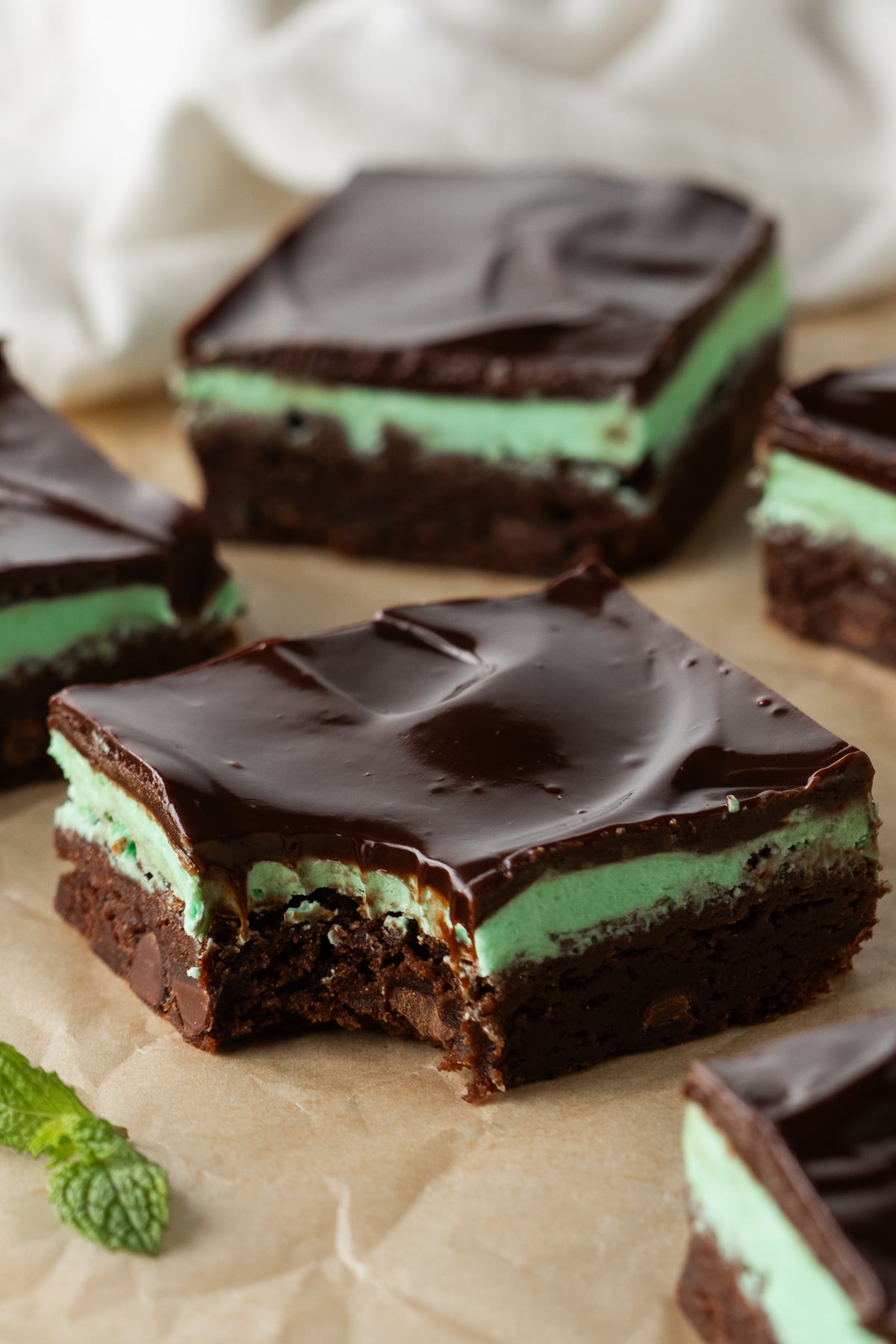 Brownies with green mint frosting and chocolate ganache on parchment with one missing a bite.