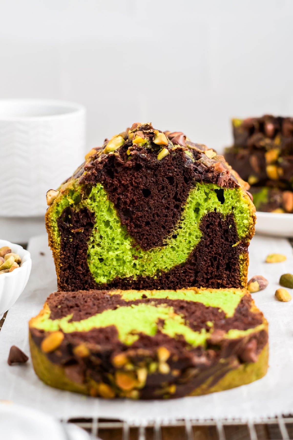 A slice cut off loaf on a platter showing the green pistachio and chocolate swirl