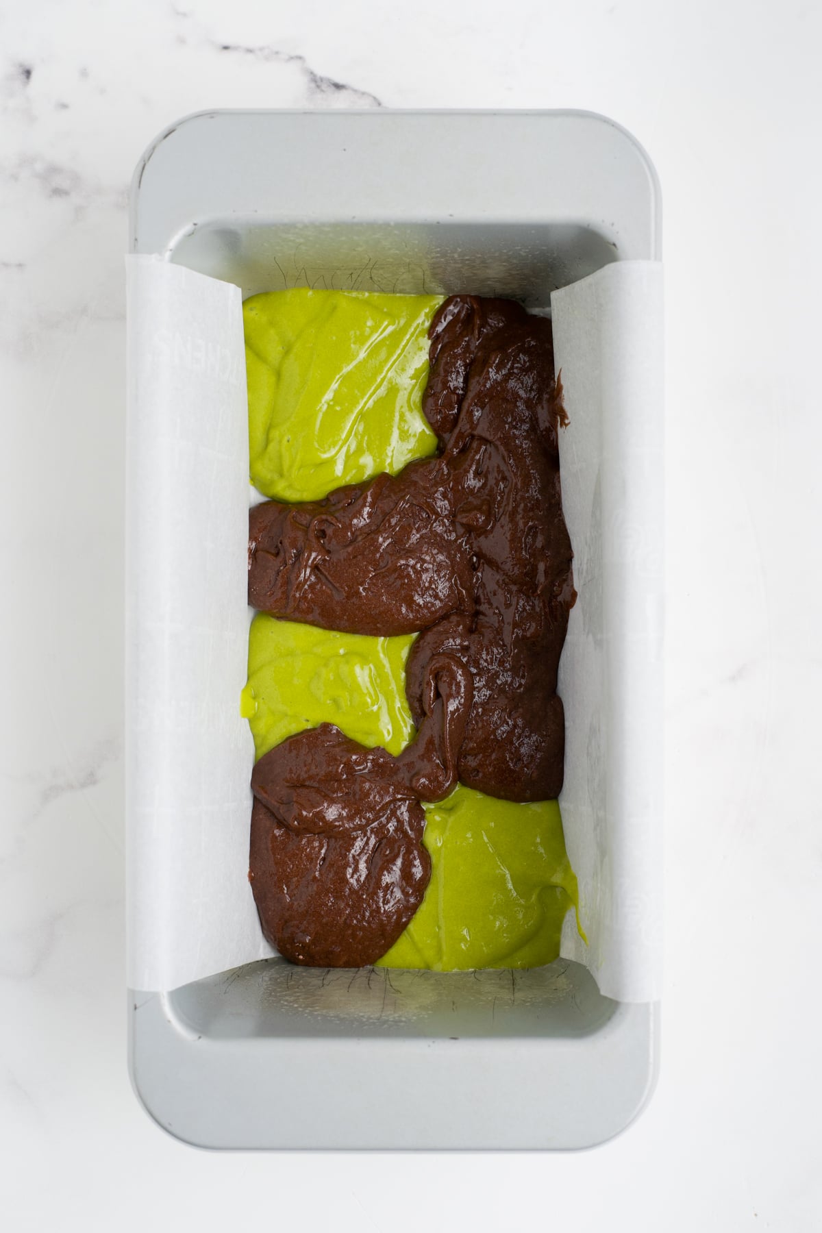 Spoonfuls chocolate and pistachio batters together in a loaf pan.