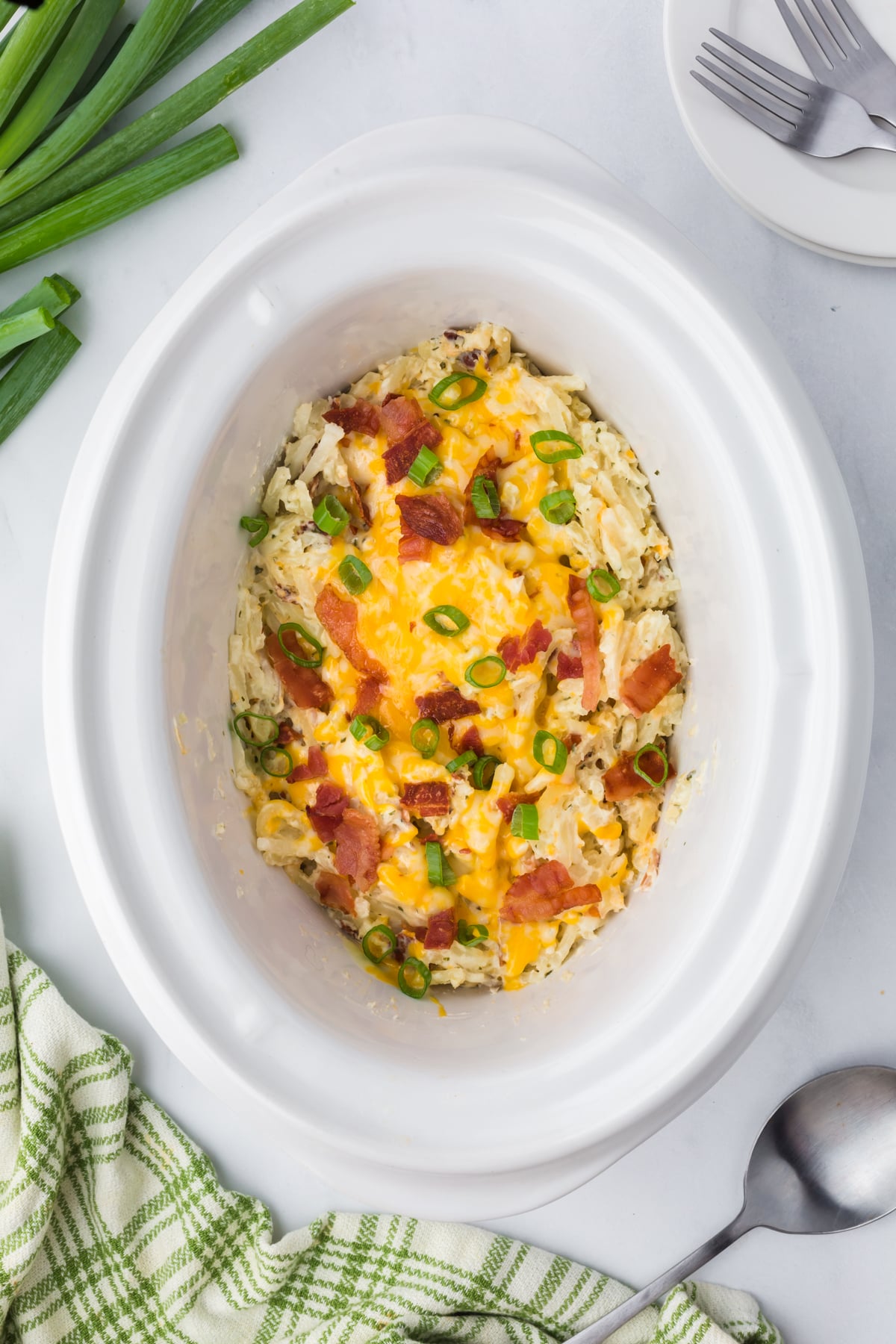 Cooked potatoes in slow cooker covered in melted cheese, bacon crumble and green onions.