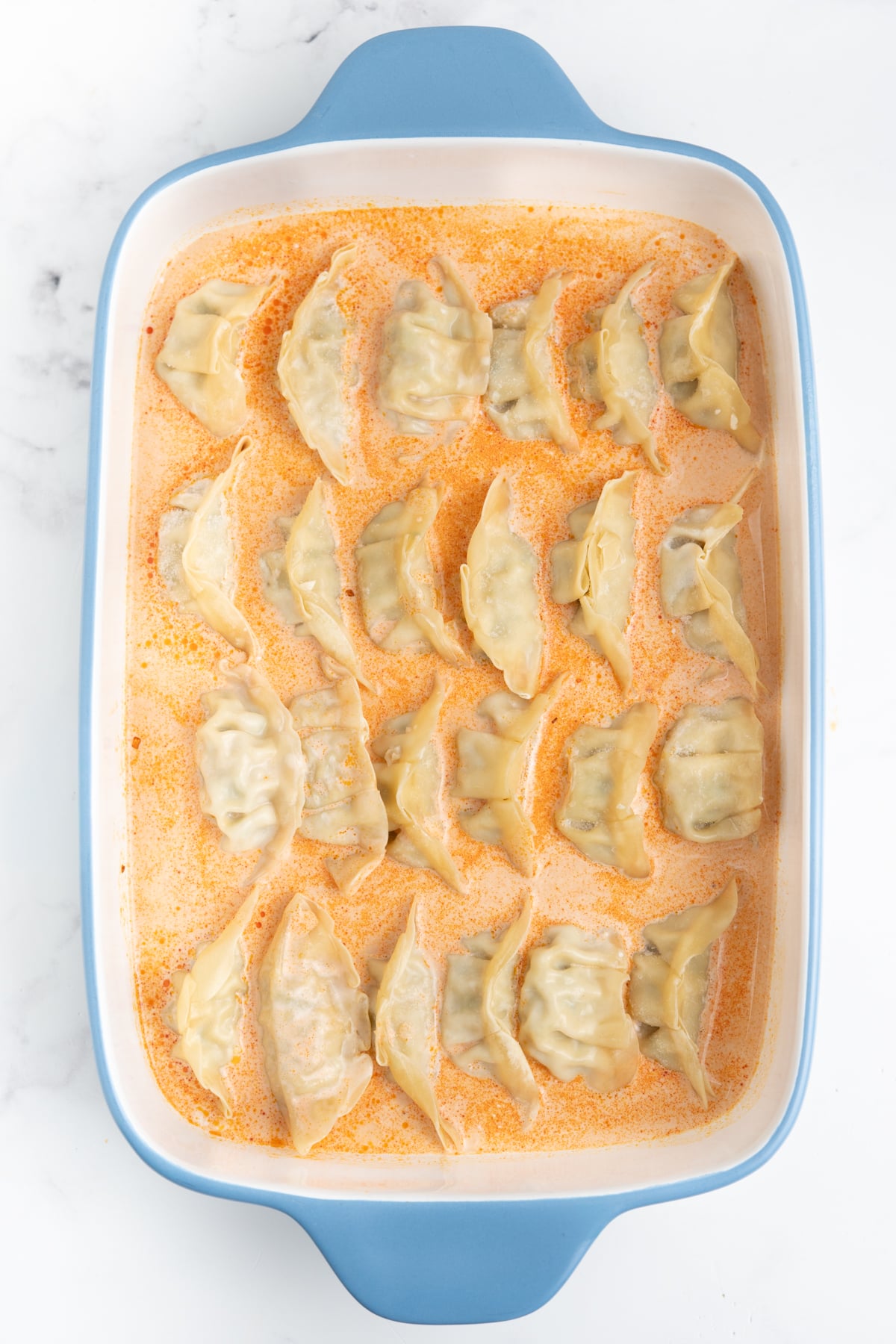 Frozen dumplings arranged in a single layer in creamy red curry coconut sauce.