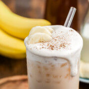 Iced Banana Bread Chai in a glass with a sprinkling of cinnamon and cold foam dripping down side.