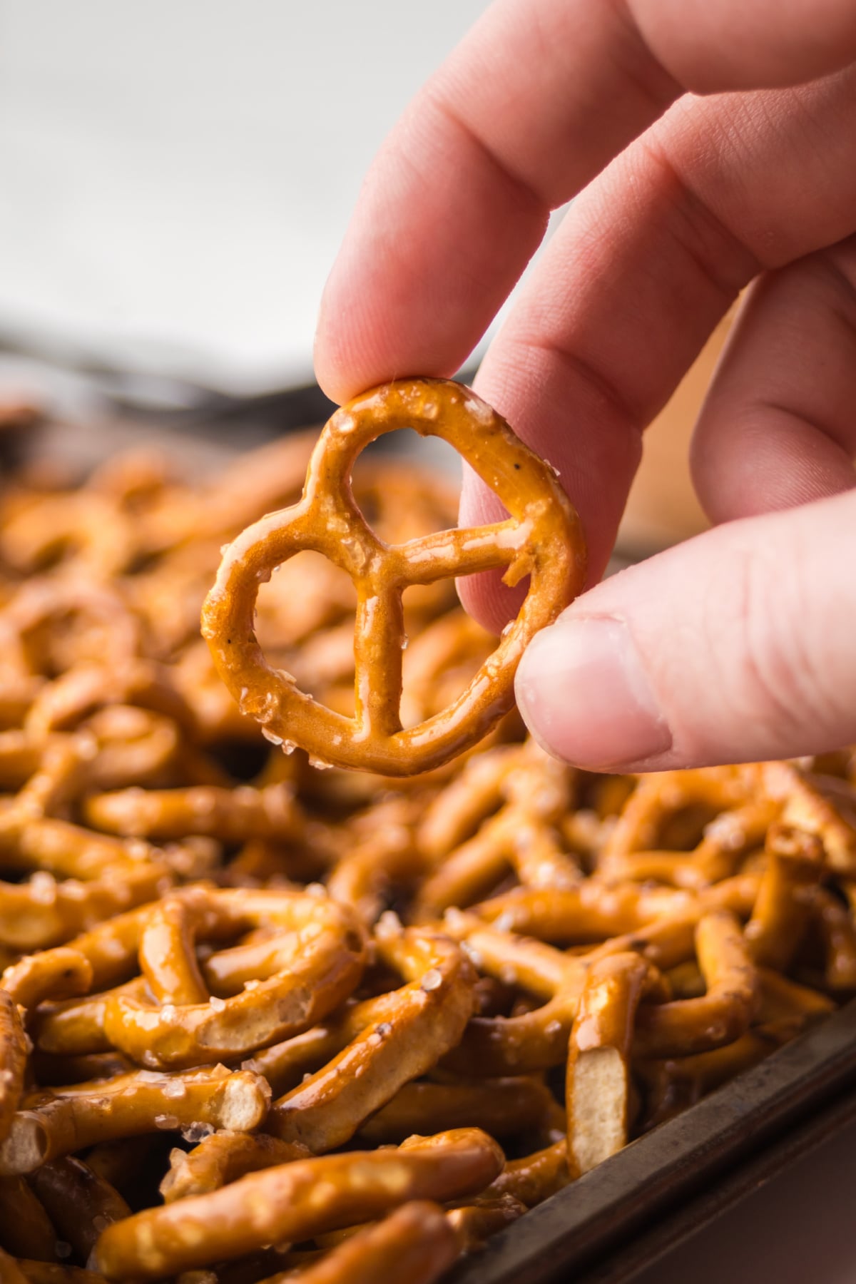A pretzel held in the air above the baking pan showing the caramel coating after baking.
