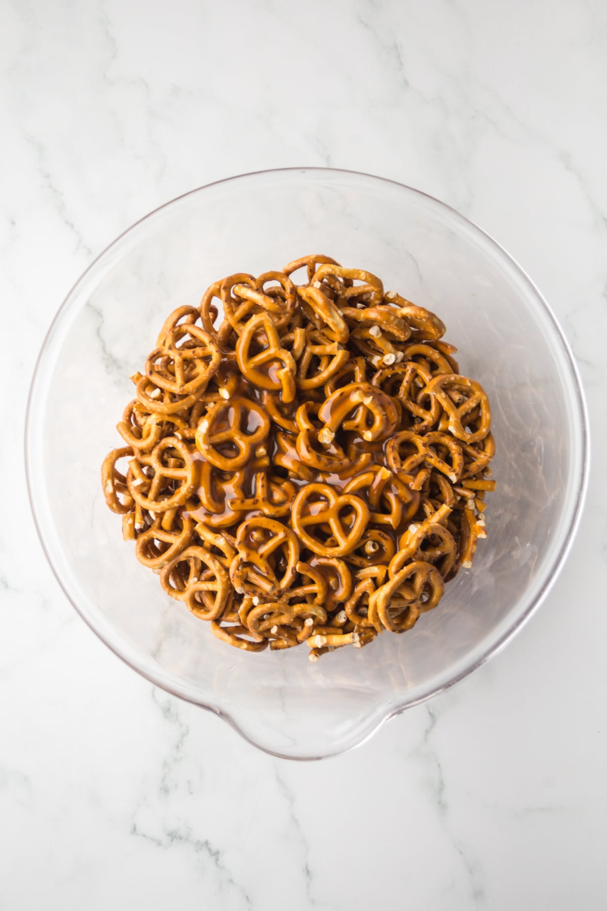 Mini pretzels being coated with caramel sauce before baking