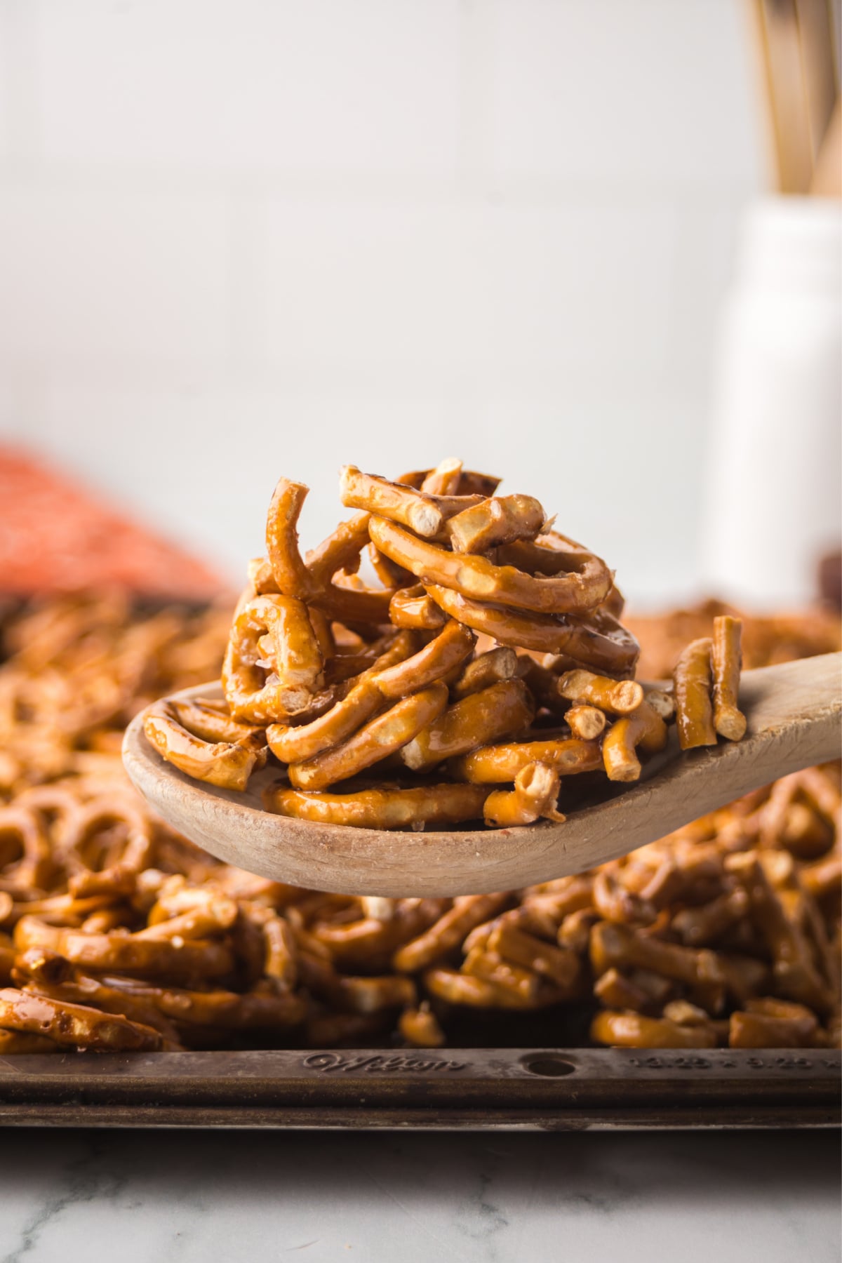 A wooden spoonful of caramel-coated pretzels held in the air after baking and cooling.