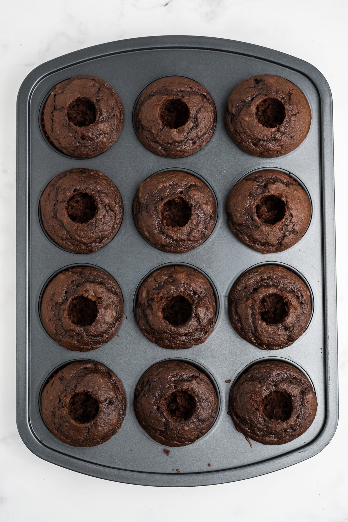 Baked cupcakes with the centers cored ready for cherries to be added.