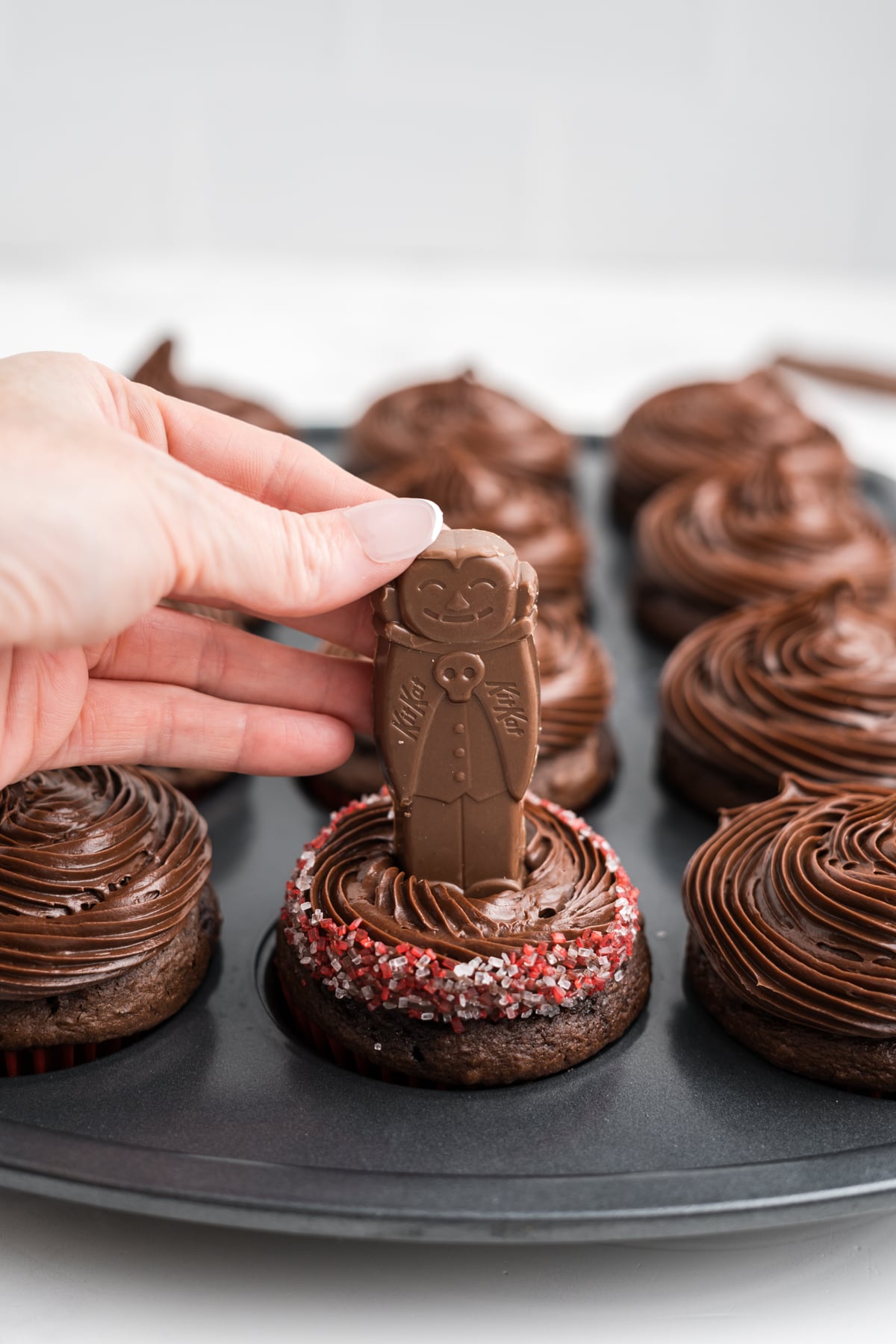Coarse sugar sprinkled on top and edge off frosting with a hand pressing a count KitKat into frosting.
