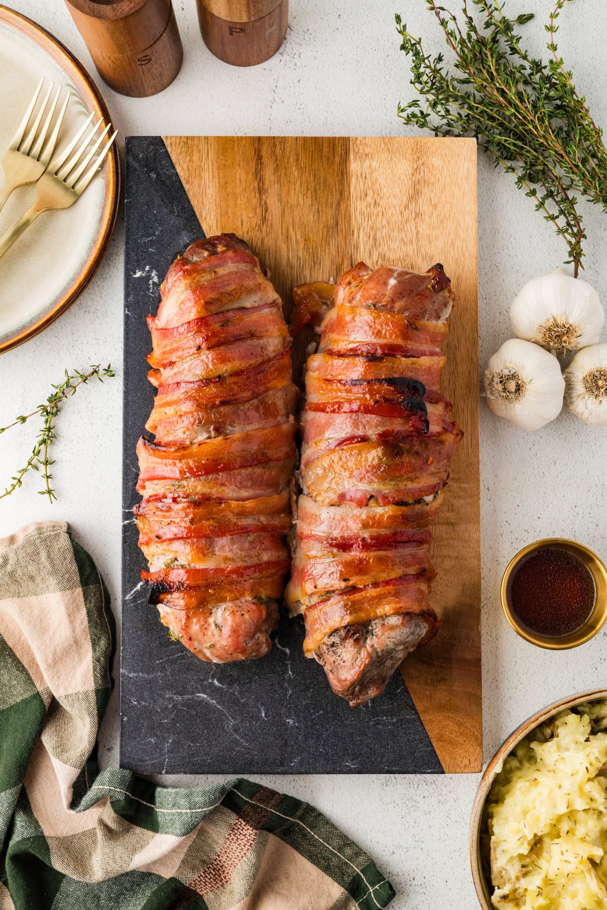 Two baked bacon wrapped tenderloins on a cutting board.