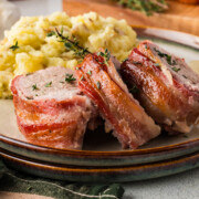 Three slices of bacon wrapped pork tenderloin with maple glaze on a plate with mashed potatoes