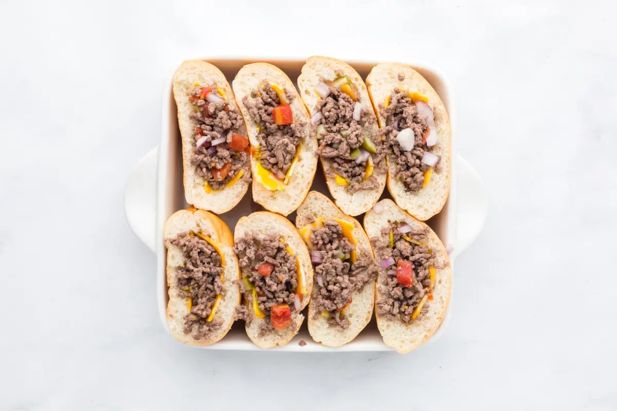 Buns in pan with ketchup, mustard and beef mixture.