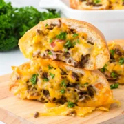 Two stacked cheeseburger rolls filled with ground beef, pickles, and melted Colby Jack cheese on a cutting board.