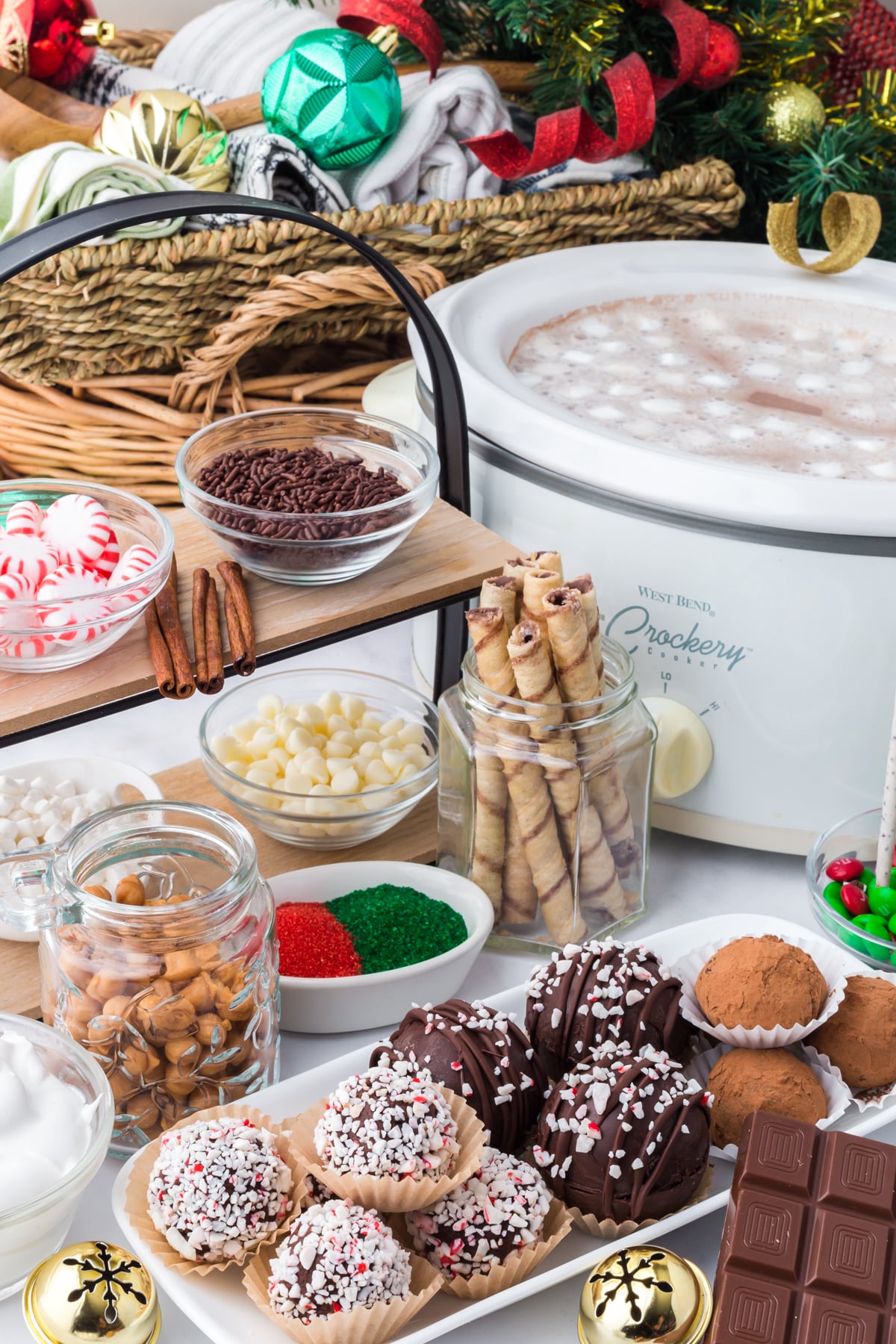 Ingredients on display in bowls on a table including a stand with bowls of treats on it and a slow cooker full of hot chocolate.