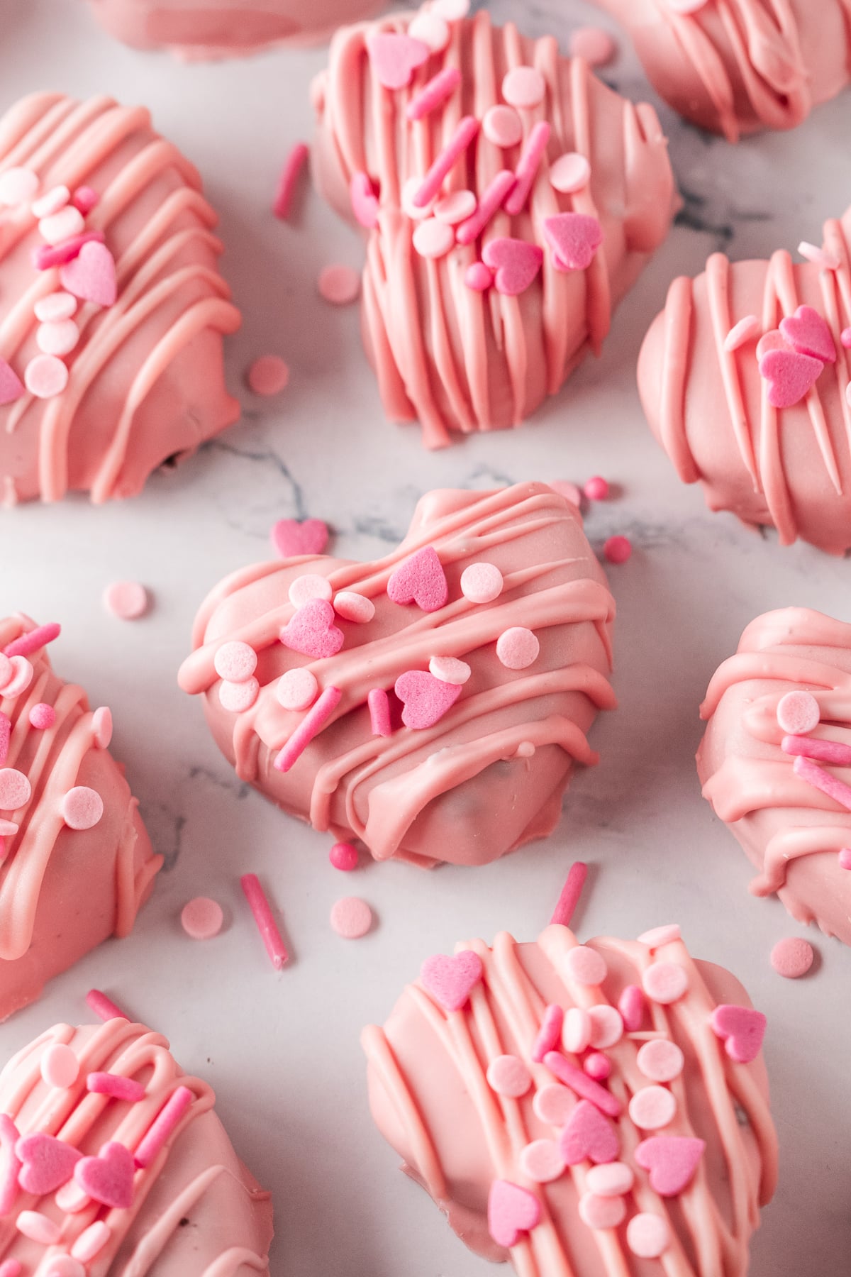 Finished pink hearts with drizzle and Valentine's Day sprinkles on parchment covered baking sheet.