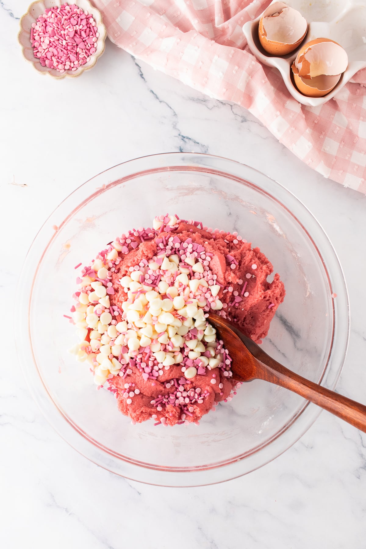 Pink cookie dough in a mixing bowl with white chocolate chips and sprinkles on top.