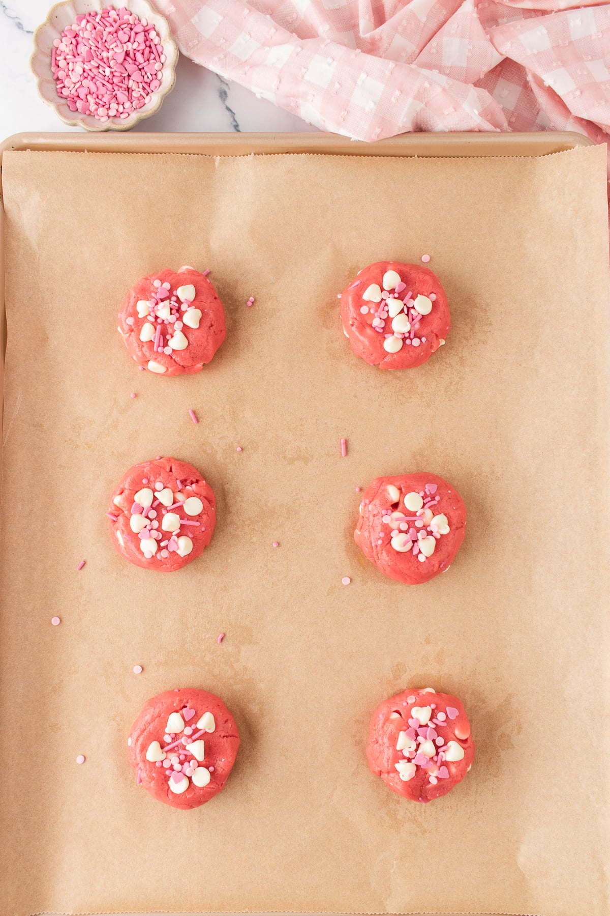 Cookie dough balls lightly flattened on parchment covered baking sheet with additional chips and sprinkles pressed on top.