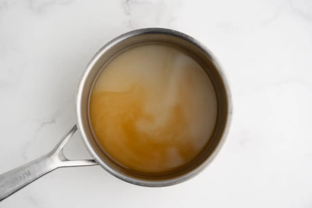Vanilla, butter, and almond extracts being added to warm syrup.
