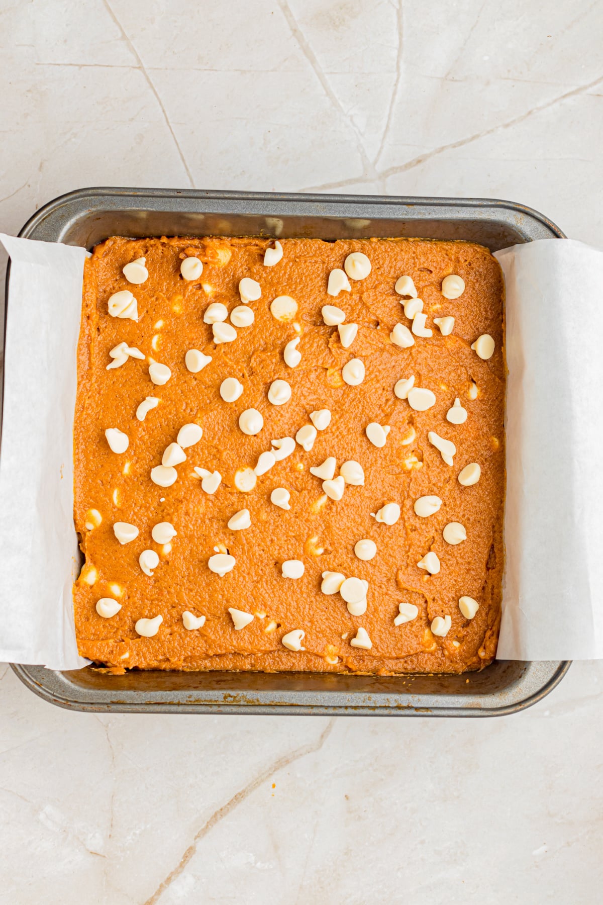 Batter in parchment covered pan with a sprinkling of chocolate chips on top.