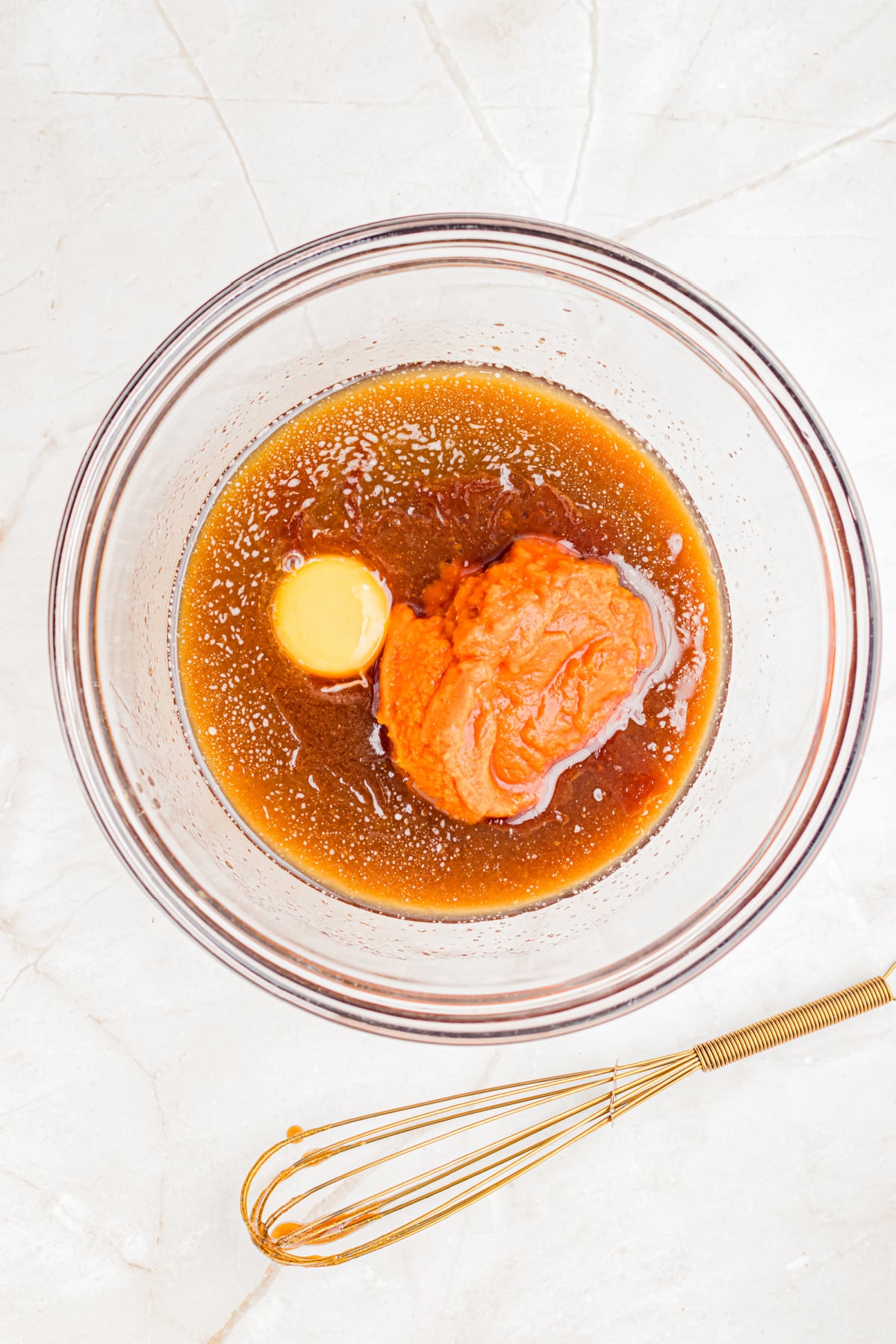 Bowl filled with melted butter, brown sugar, egg yolk, pumpkin puree, and vanilla and a whisk.