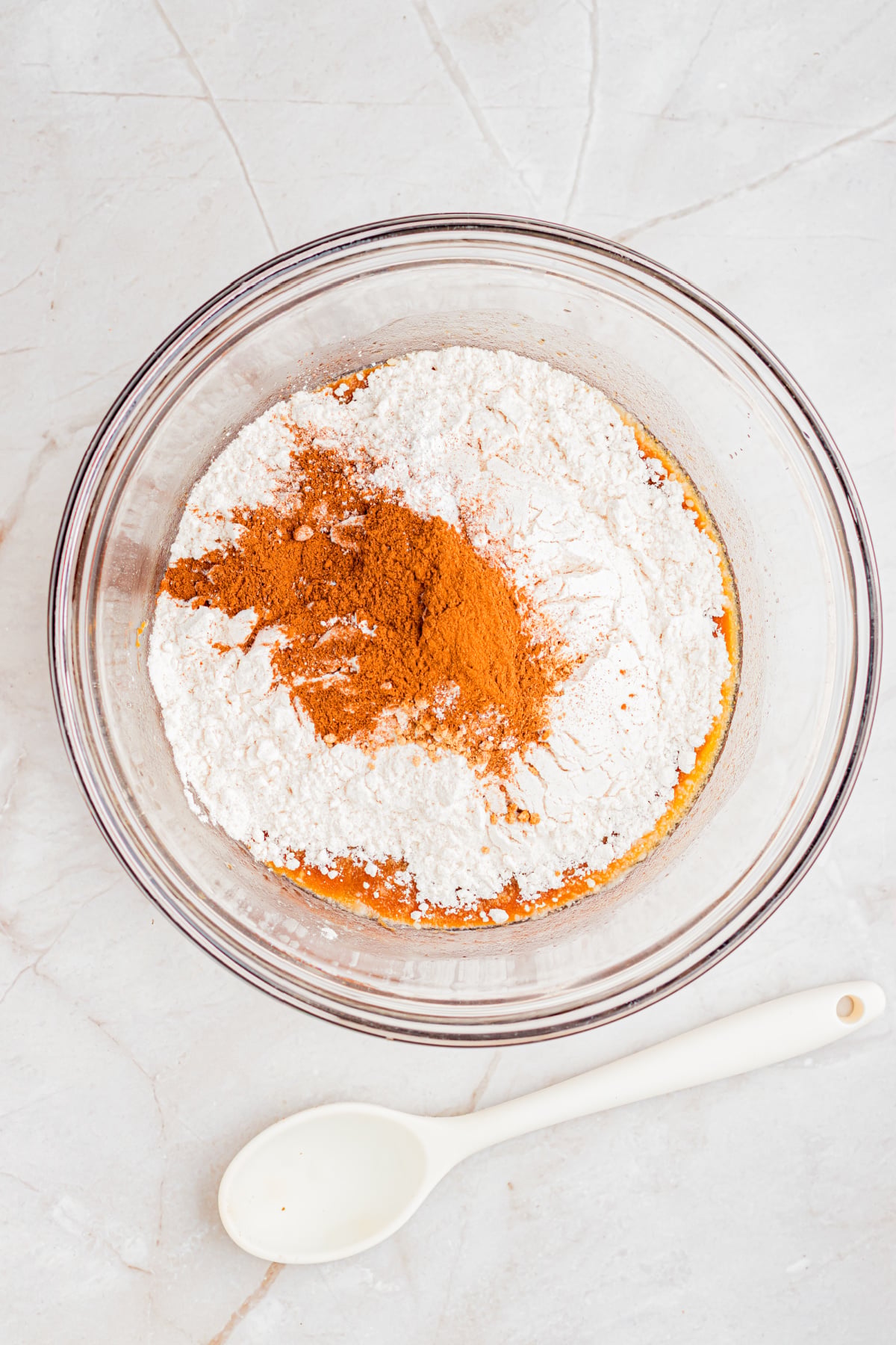 Flour, cinnamon, ginger, nutmeg, baking powder, and salt added to the bowl with a spoon.