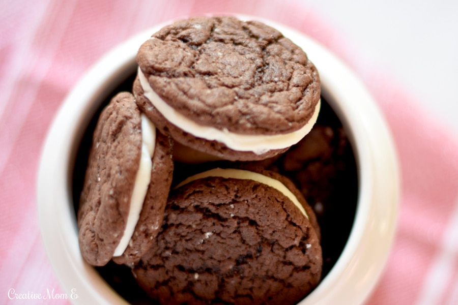 Looking down at chocolate sandwich cookies in a cookie jar on top of a red tea towel.
