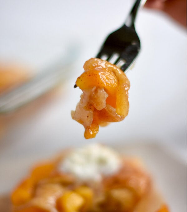 Fork filled with peach cobbler with a big gooey peach.