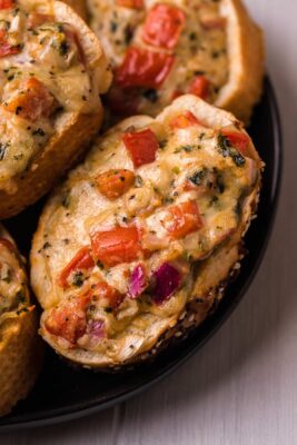 Closeup of cheesy bruschetta bites on a black colored plate.